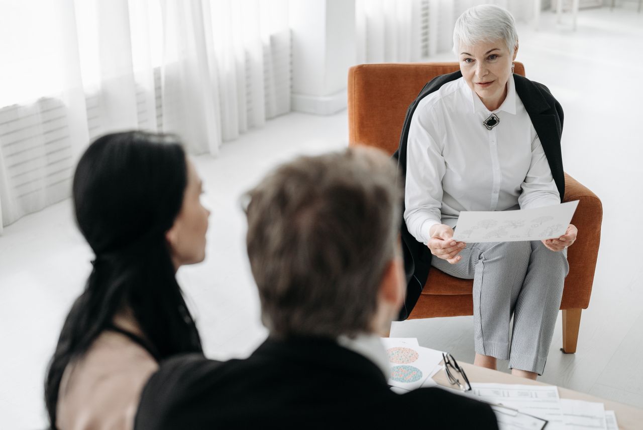 Professional advisor discussing documents with a couple in a modern office setting.